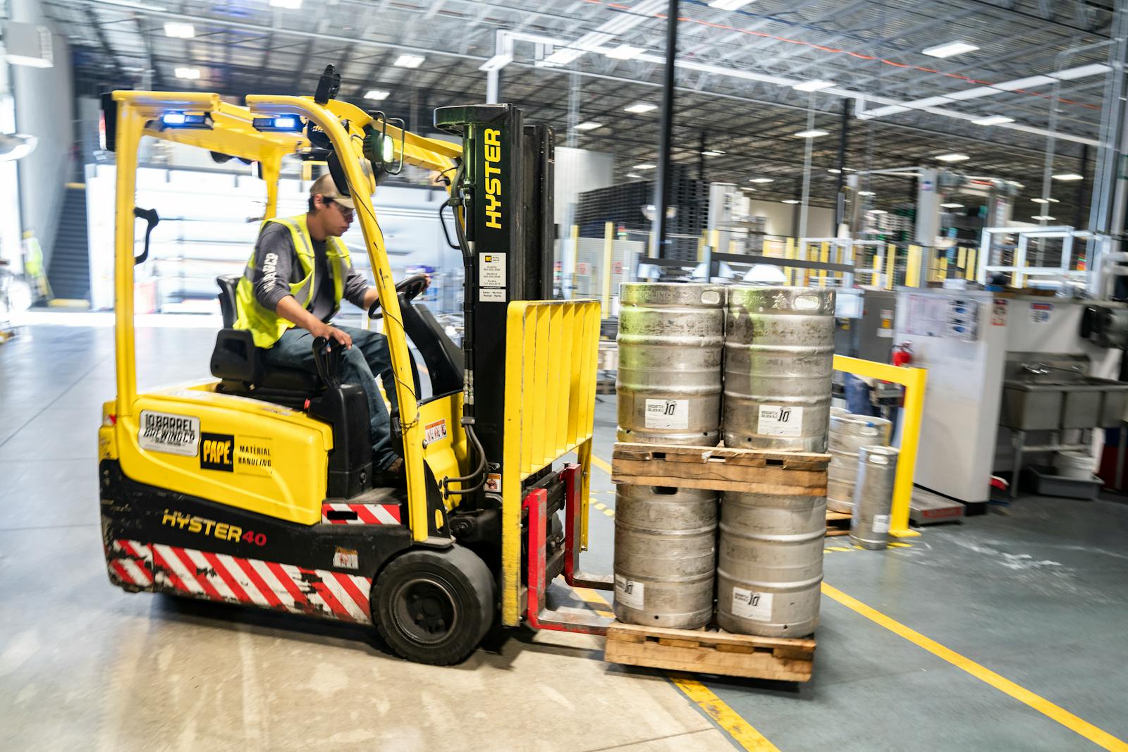 Forklift operator in warehouse moving beer kegs for distribution.