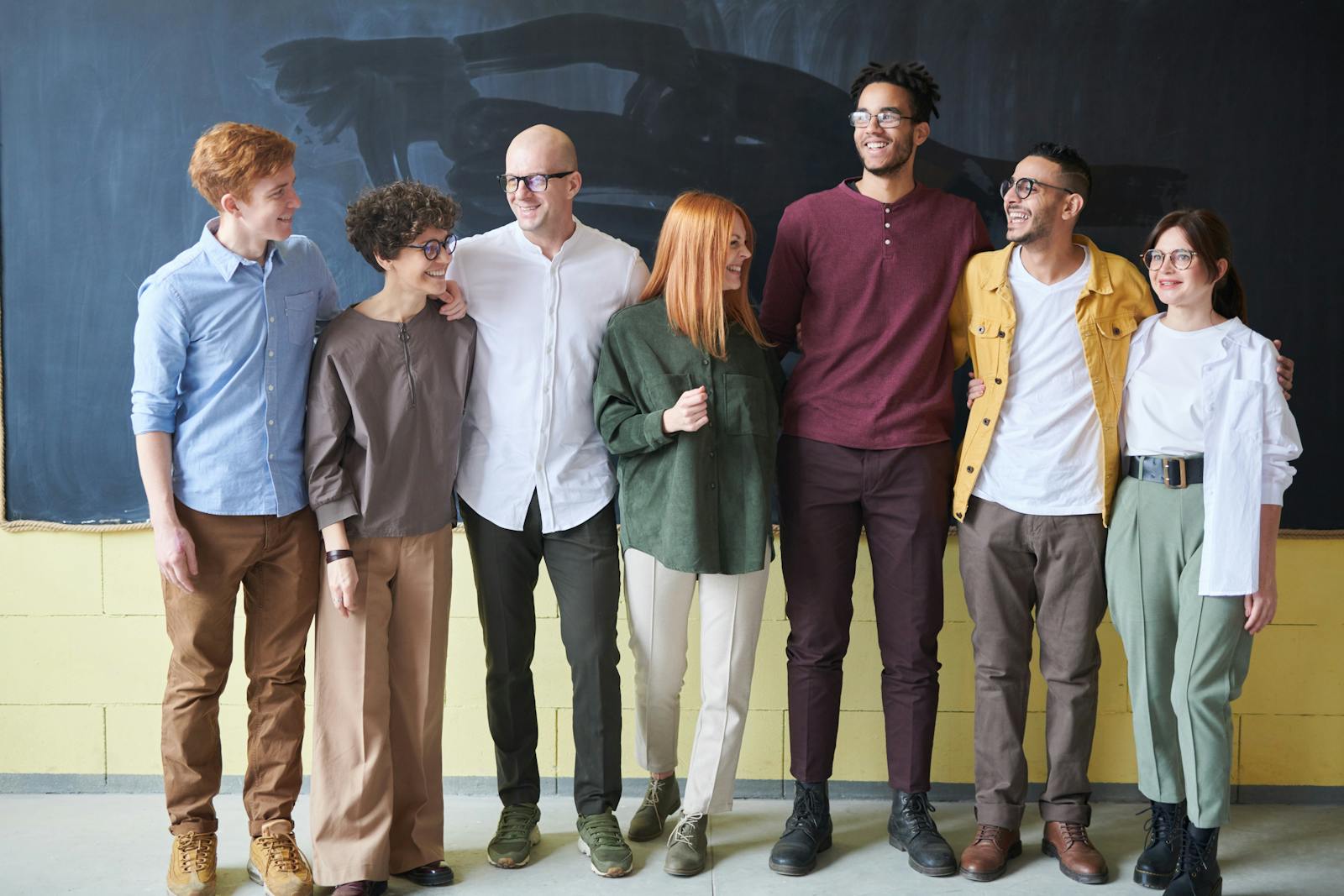 A multicultural group of six adults standing happily together in a casual setting.