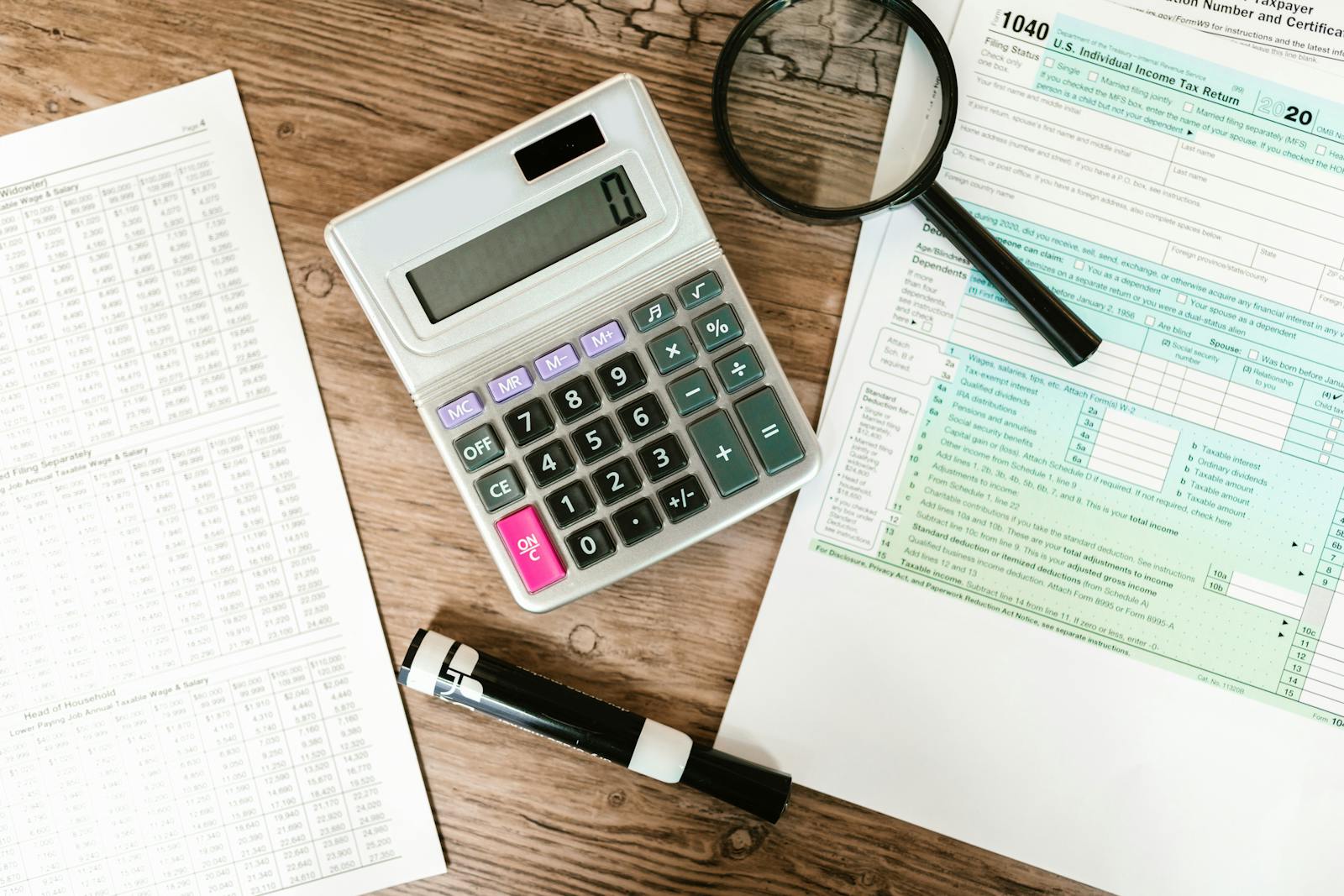 Top view of tax forms, a calculator, and a magnifying glass on a wooden surface, ideal for accounting themes. BOI