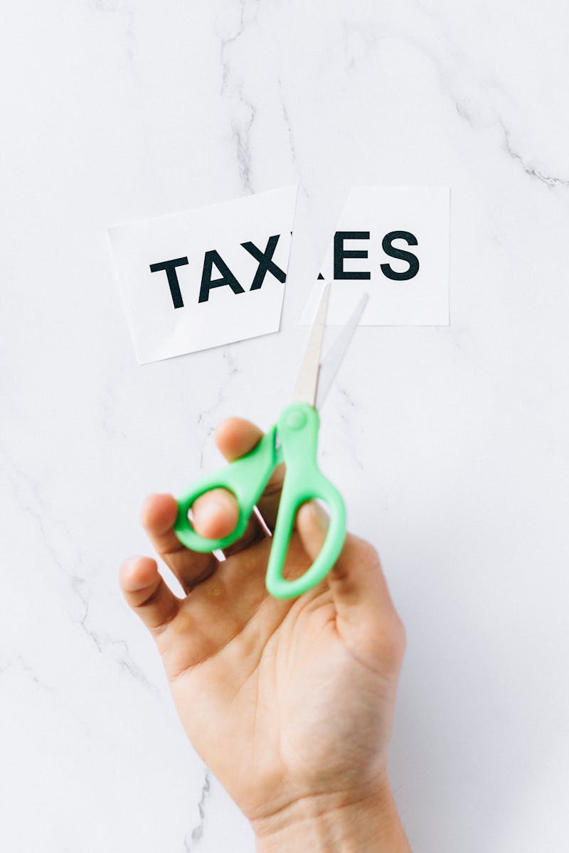 Top-down view of a hand holding scissors cutting the word 'taxes' on a marble surface.