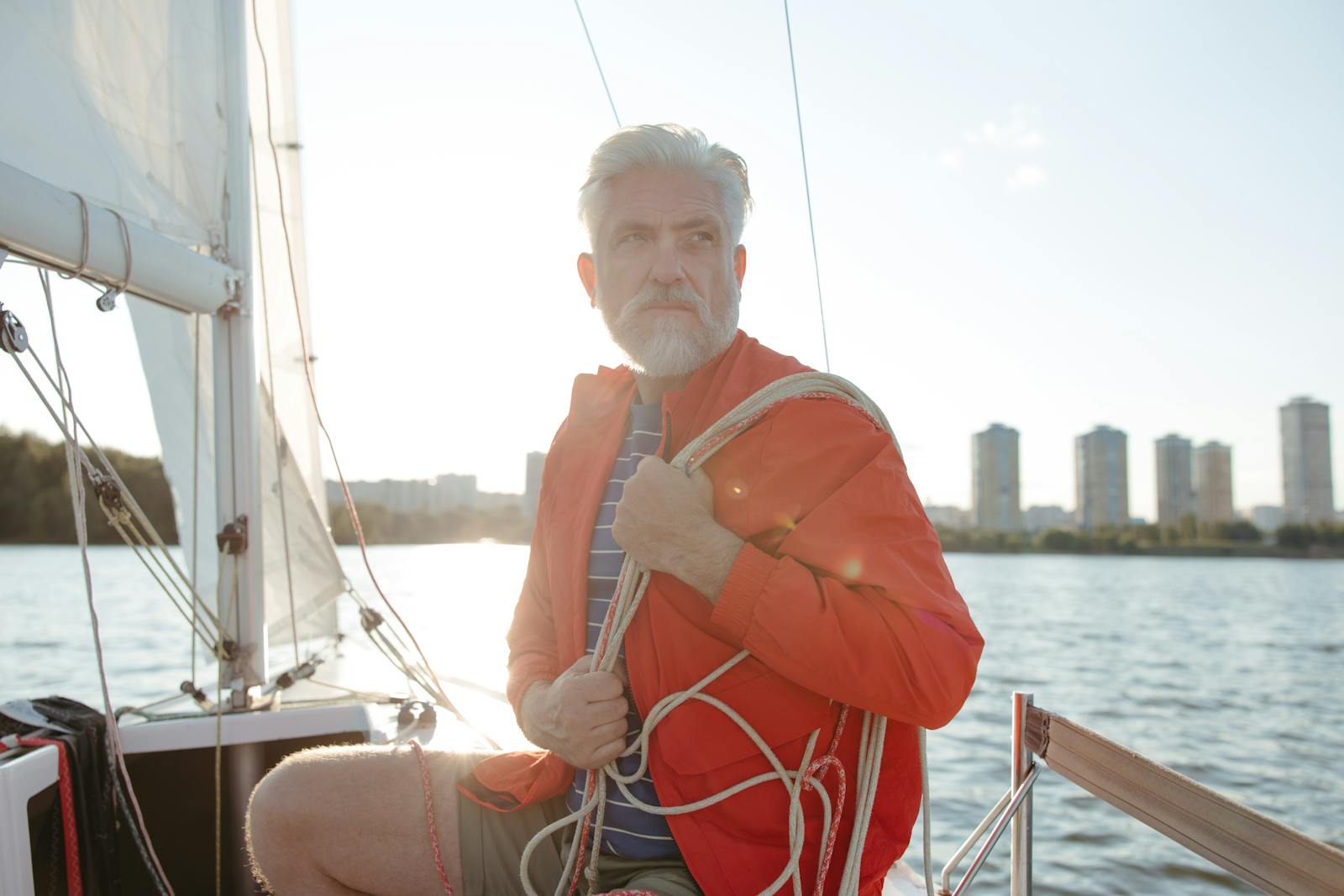 Retired Senior man enjoying a sunny day sailing on a yacht by the city waterfront.