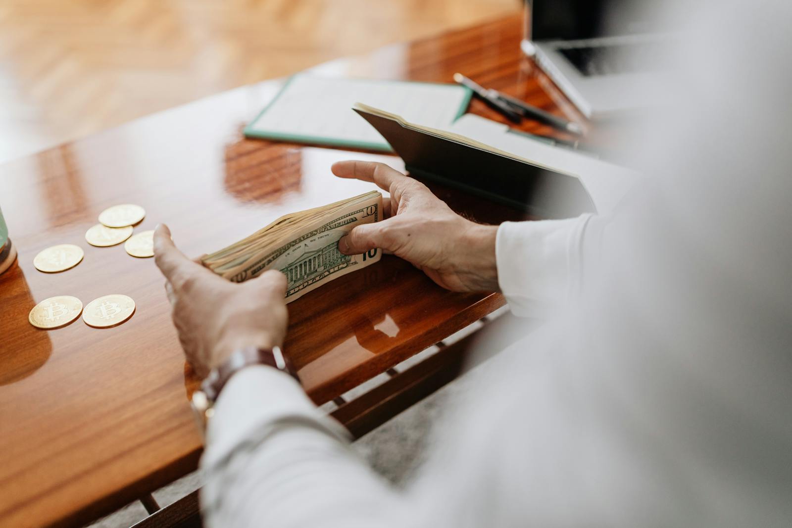 Person counting cash and coins on a wooden table, emphasizing financial tasks. CFO